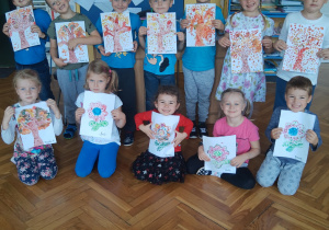 W dniu "kropki"grupa uśmiechniętych dzieci prezentuje w swojej klasie prace plastyczne wykonane farbami. Prace przedstawiają kolorowe drzewa i kwiaty.